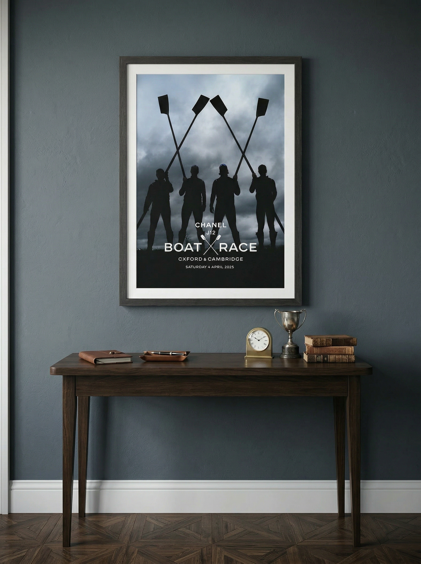 Framed poster of silhouettes with oars on a dark wall above a wooden table.