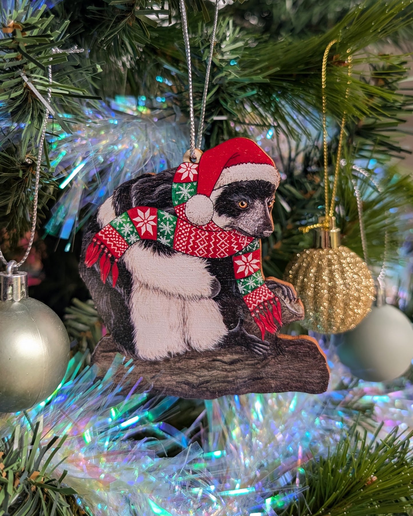 Decorative Christmas ornament of a lemur wearing a Santa hat and scarf on a tree.