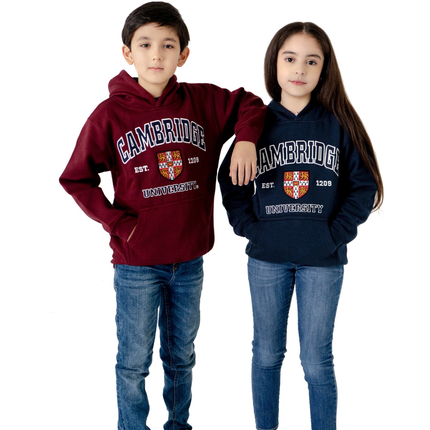 Two children in hooded sweatshirts, one maroon and one navy. Design on front of sweatshirts includes the University of Cambridge shield, lettering above and below the shield that reads CAMBRIDGE and UNIVERSITY in capitalised serif font outlined in white, and EST. 1209 in white. Brought to you by CuratingCambridge.com