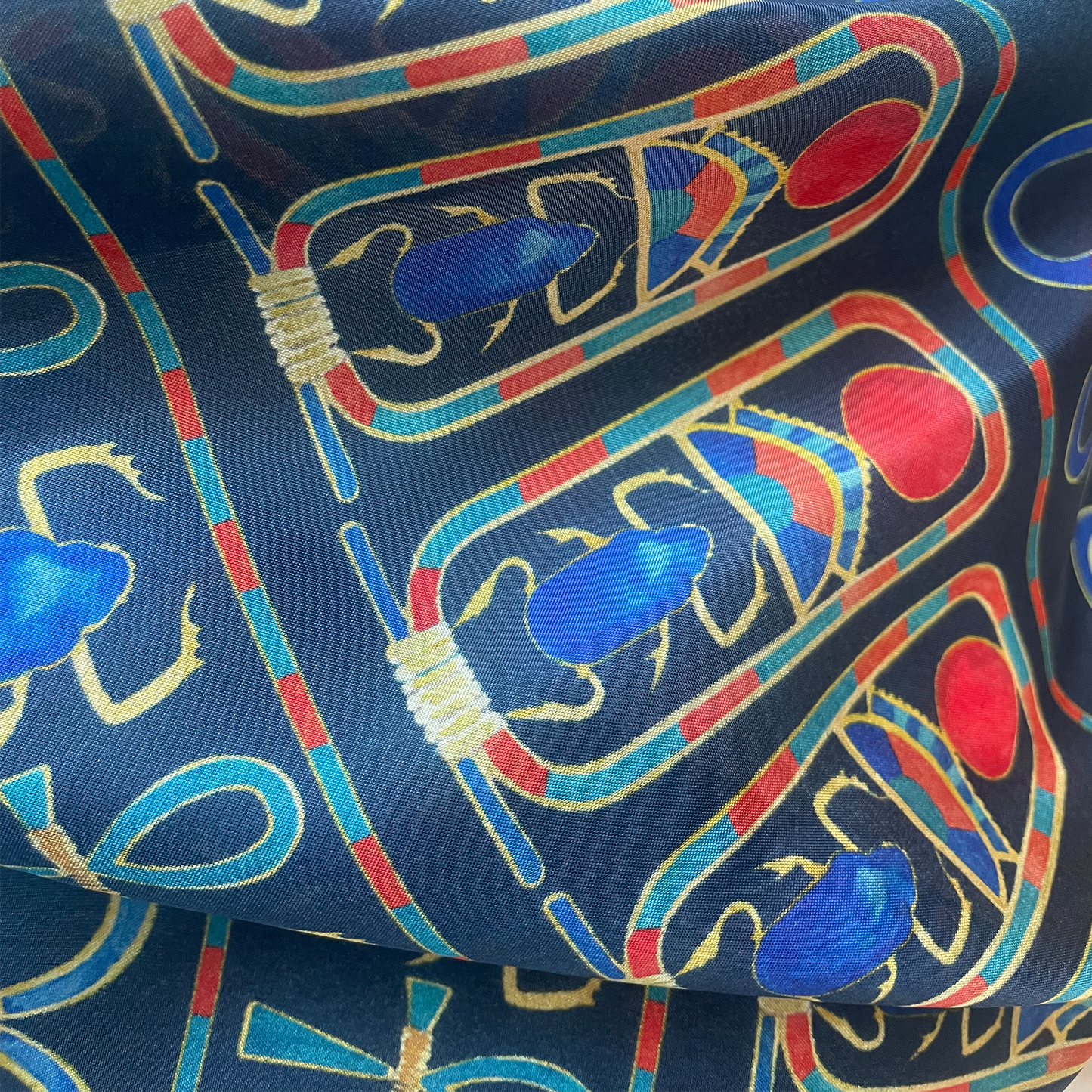 Fabric with colorful Egyptian-style pattern featuring blue, red, and gold on a dark blue background.