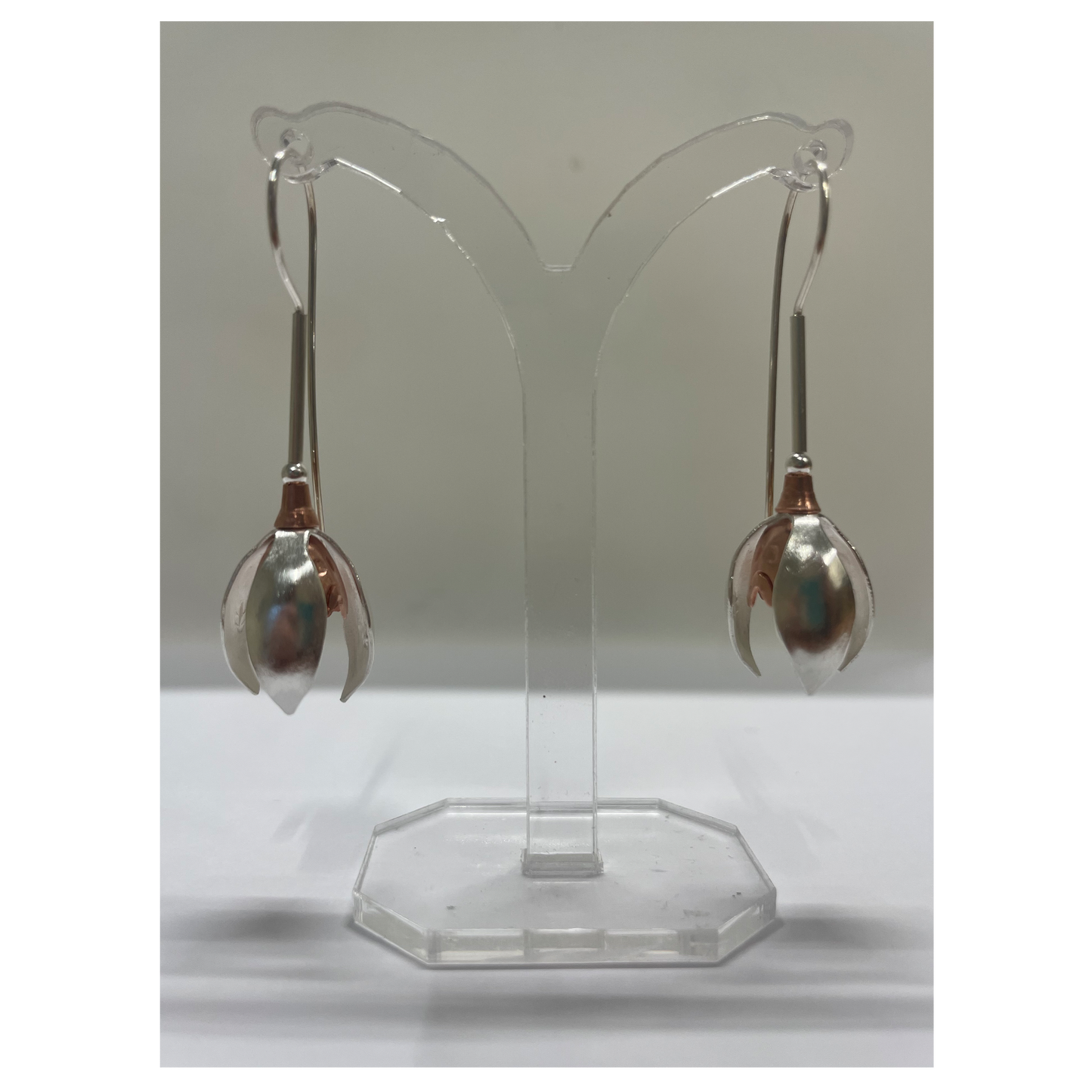 Pair of silver earrings on a clear stand against a white background