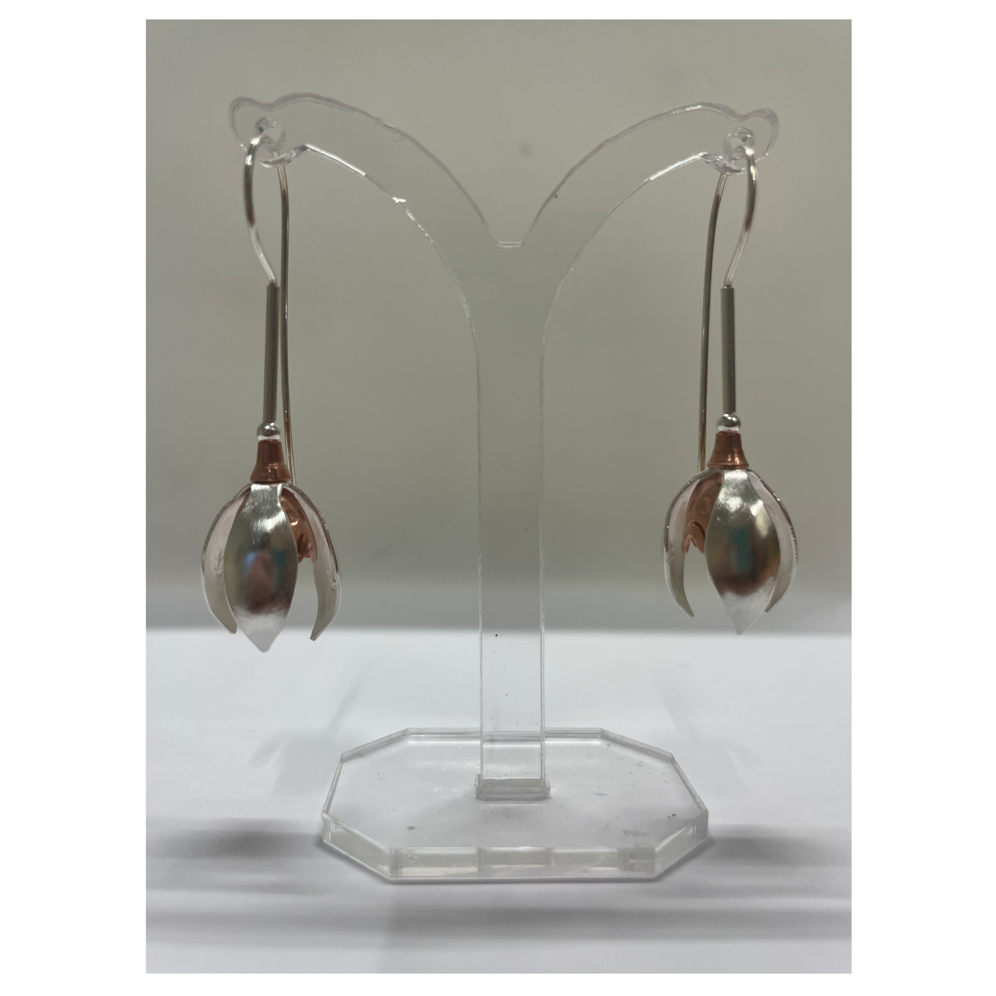 Pair of silver earrings on a clear stand against a white background