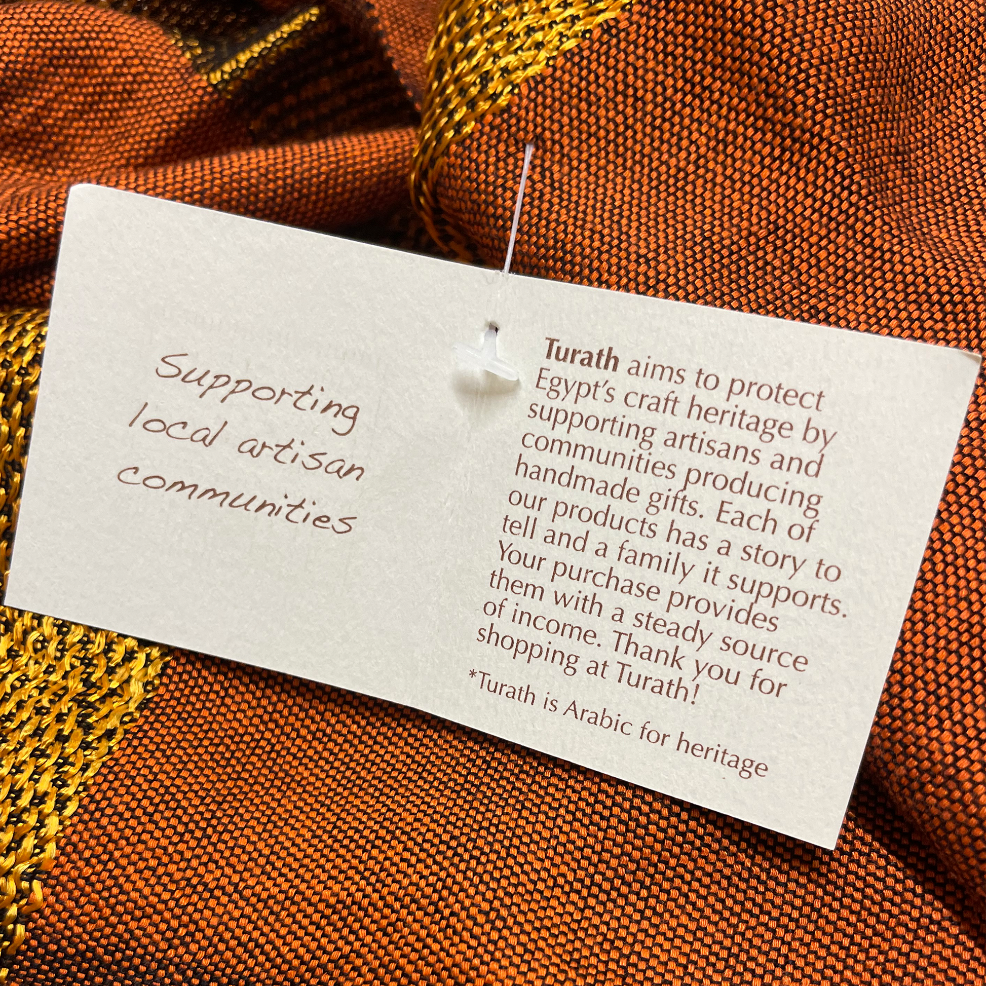 Textile with a Turath tag on an orange fabric background