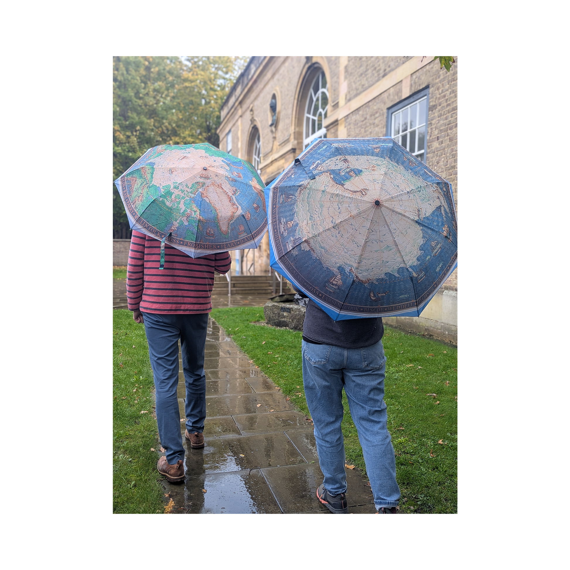 Two people holding world map umbrellas in a park setting.