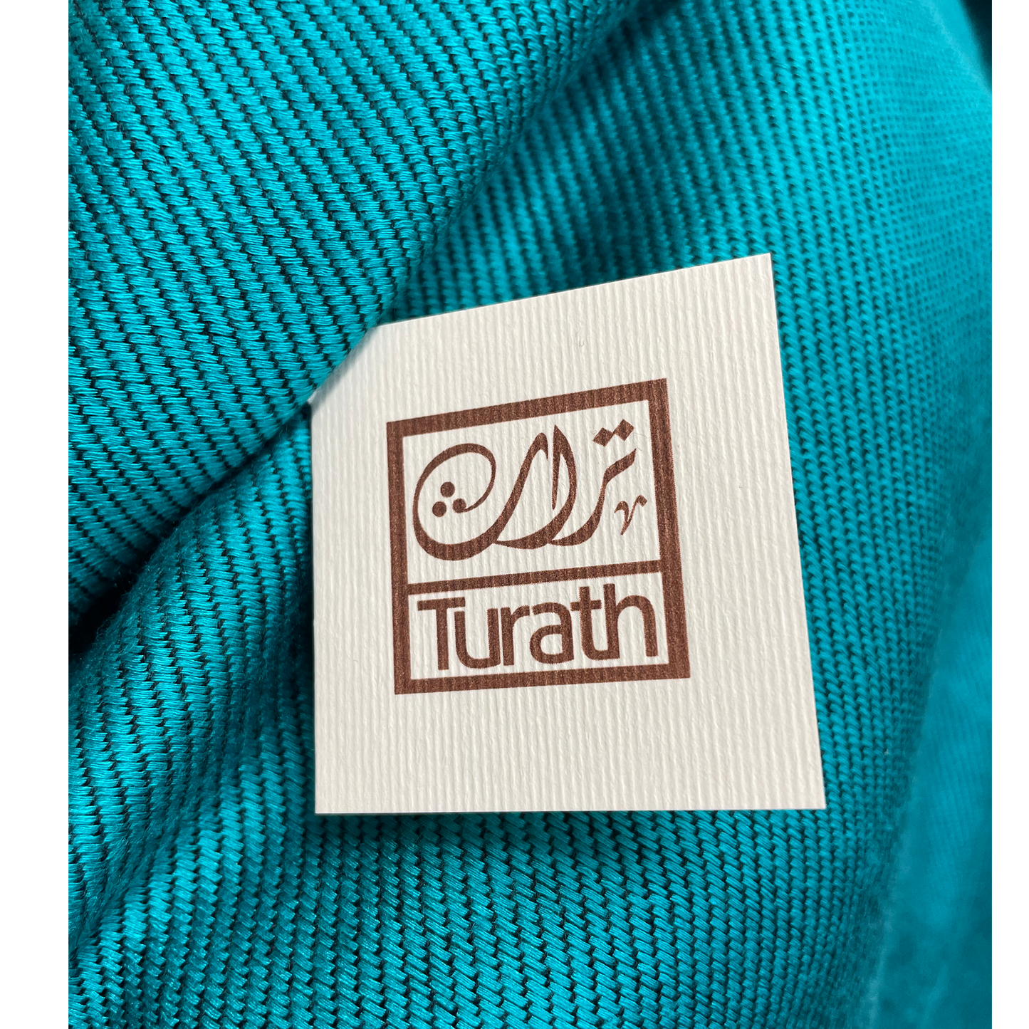 Turath label on a teal fabric background
