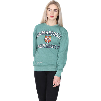 Female model wears sweatshirt in Cambridge blue (pale green). Sweatshirt has the Cambridge University coat of arms on the front, with the word CAMBRIDGE above and UNIVERSITY below, in white serif font capitals outlined in black. White italic text at the bottom right of the sweatshirt reads Est. 1209. Brought to you by CuratingCambridge.com